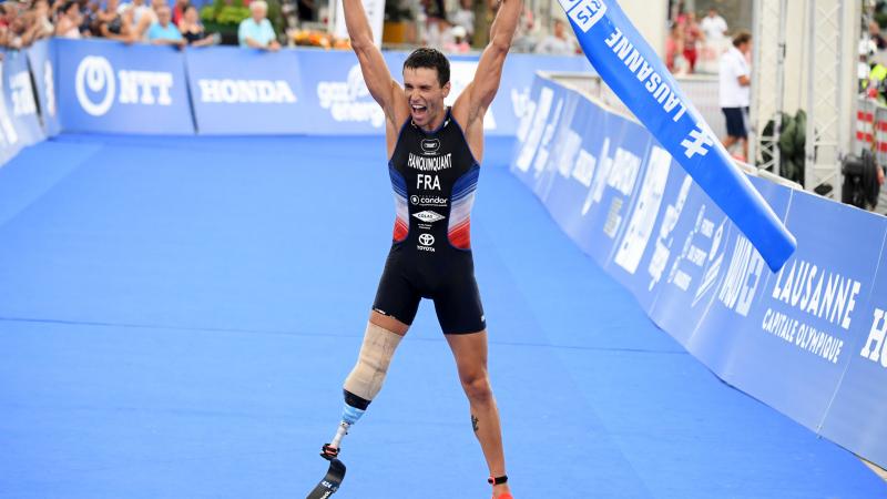 French man with right leg impairment lifts tape over head celebrating a win