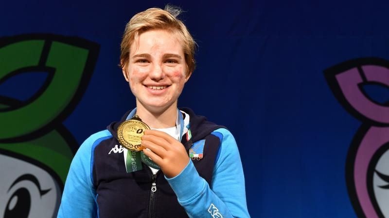 Female fencer smiles holding gold medal