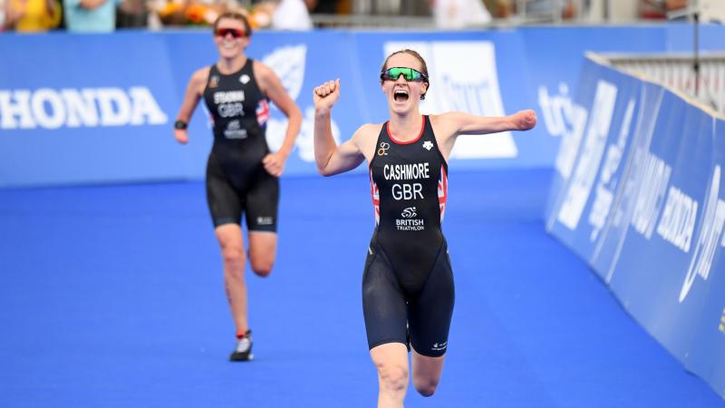 Female triathlete with arm amputation celebrates with opponent in background smiling