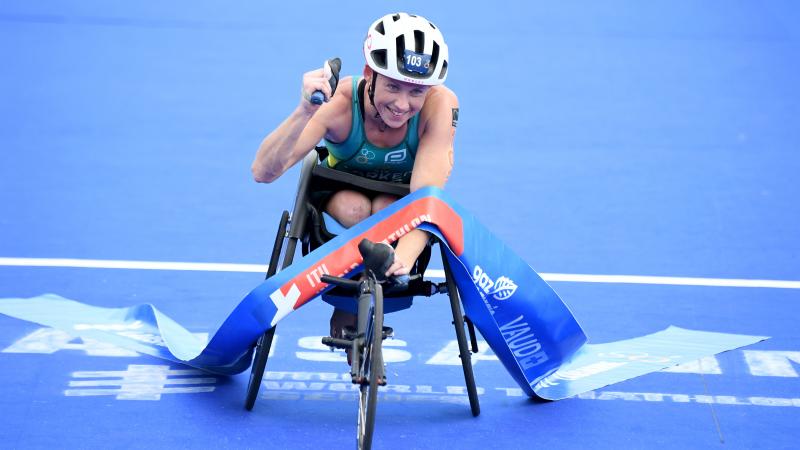 Woman in racing chair crosses finish line tape