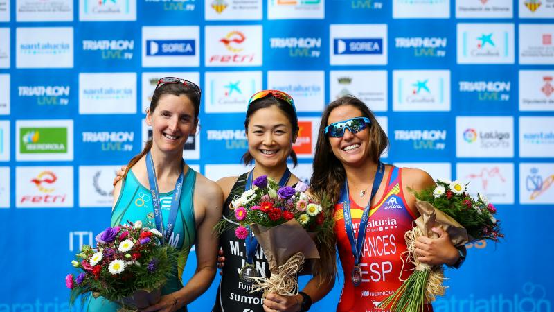 Three female Para triathletes pose together on the podium