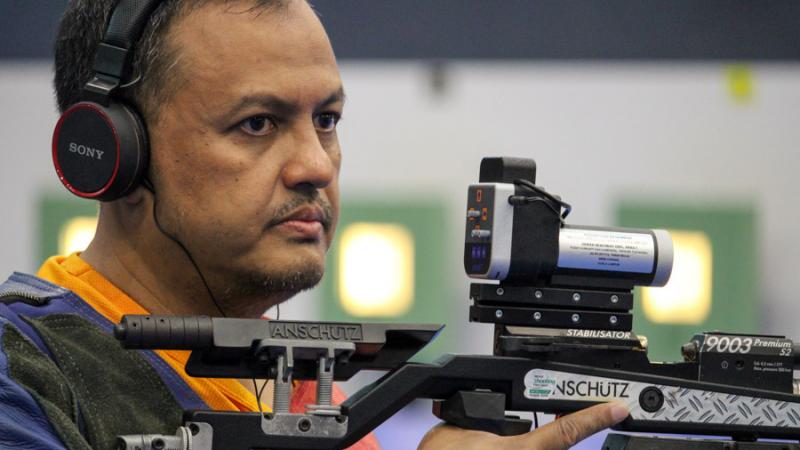 Male shooting athlete with headphones looks on while holding rifle