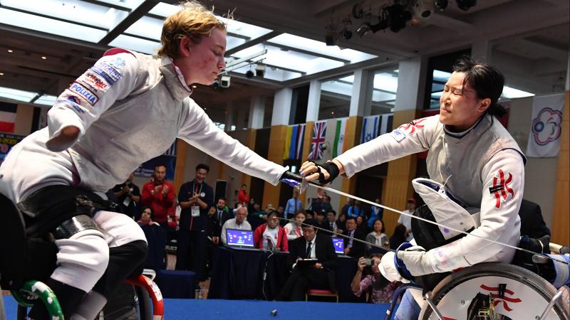 Two female wheelchair fencers reach over to shake hands