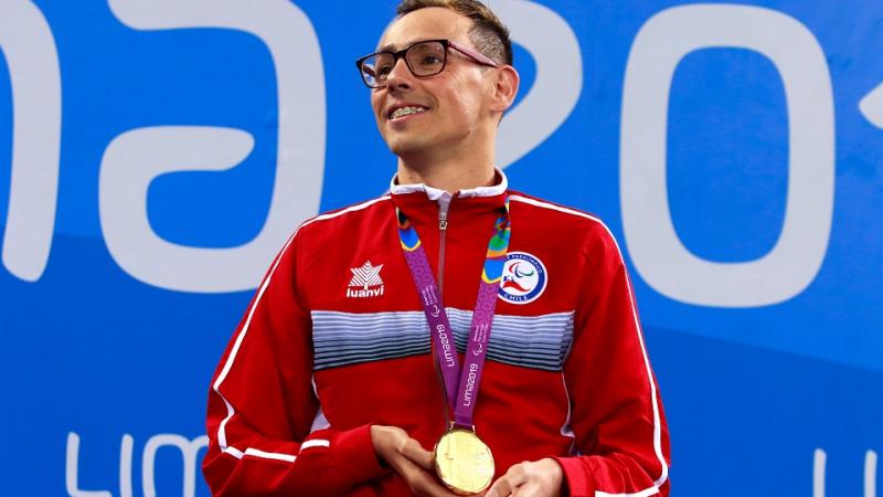 Chilean swimmer Alberto Abarza on the podium smiling and holding his gold medal