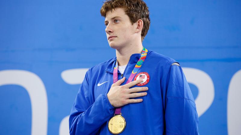 US swimmer Carson Sanocki on the podium with his hand on his chest and the gold medal hanging around his neck