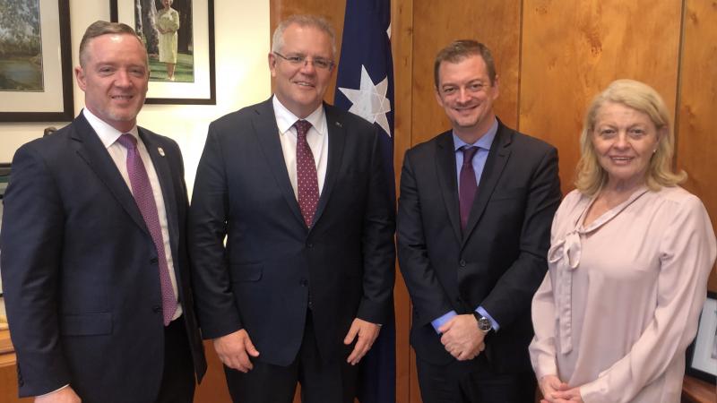 Three men and a woman posing for a picture with a flag of Australia behind them