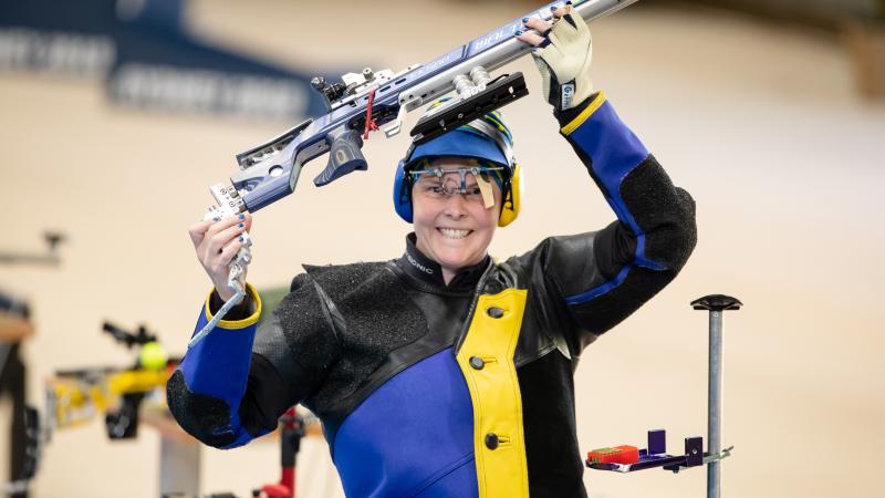 A female shooter smiling a holding her rifle above her head