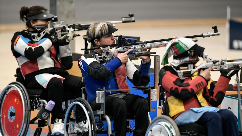 Three female shooters in wheelchairs competing with rifles