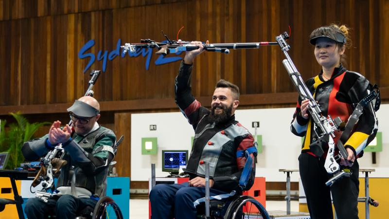 Rifle shooting medallists with gold medallists listing rifle above his head