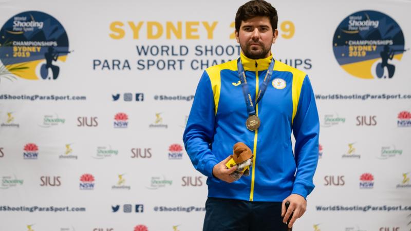 Ukrainian man stands with gold medal around neck and prize in hand