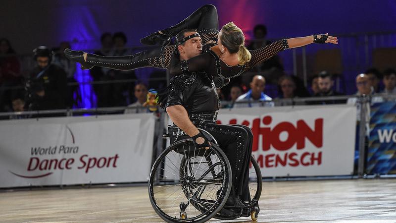 Male wheelchair dancer lifts female dance partner on shoulders