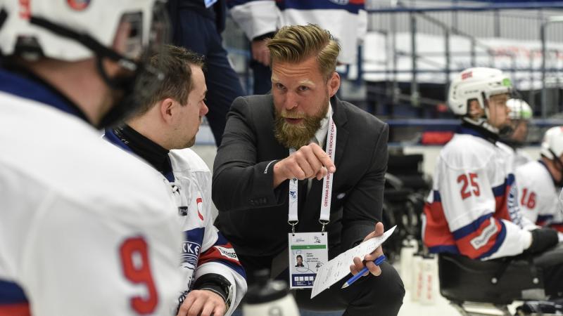 A man in suit talking to a Para ice hockey player on the ice