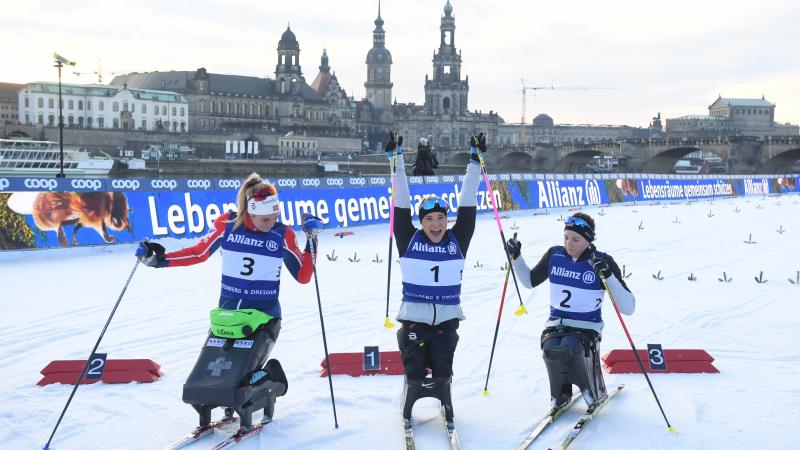 A female sit-skier celebrating between two other skiers