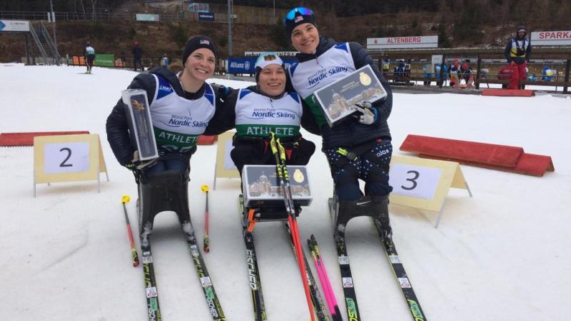 Three female sit-skiers posing with their trophies