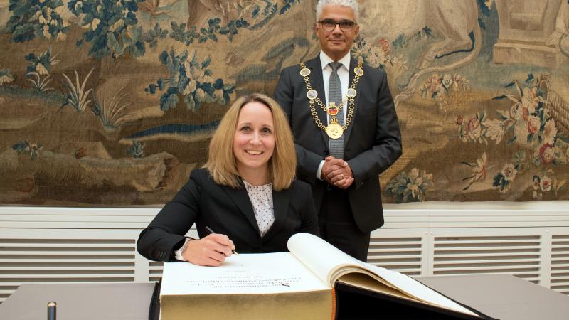 Female German athlete in wheelchair signing a book with mayo standing behind