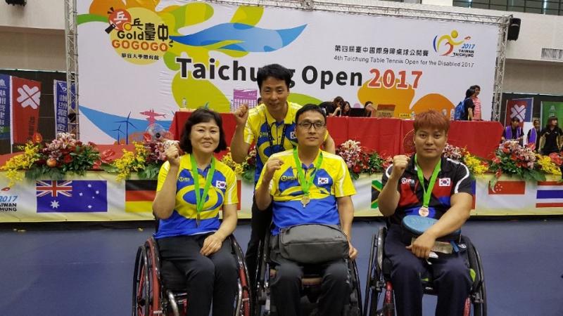 Three Korean table tennis players in wheelchairs and their coach pose