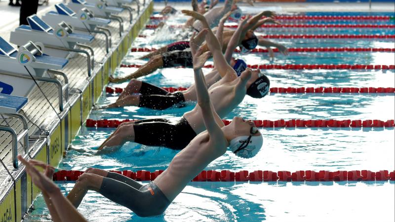 A group of male swimmers jumping in the water for a backstroke race