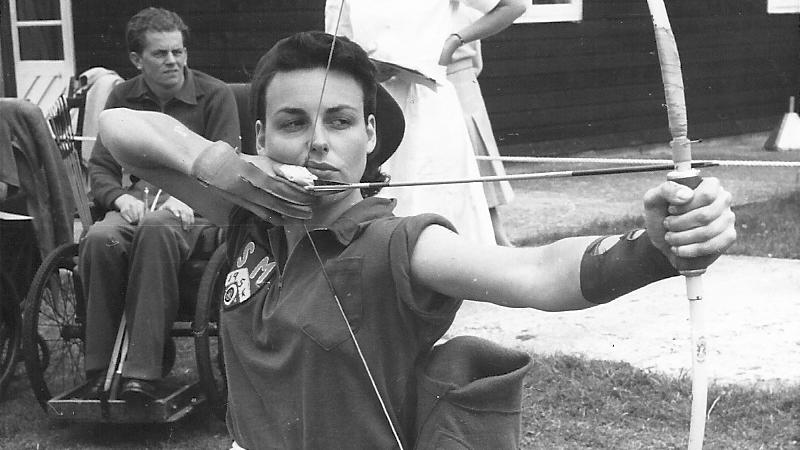 Black and white photo of woman aiming her bow and arrow