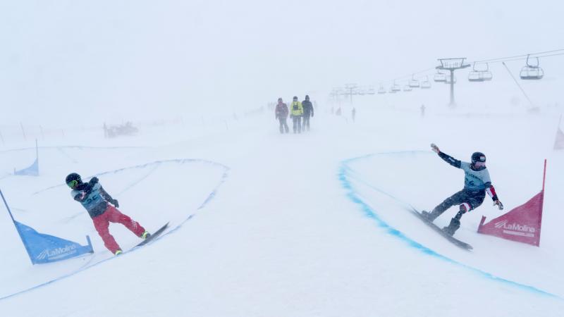 Two male Para snowboarders competing under heavy snowfall