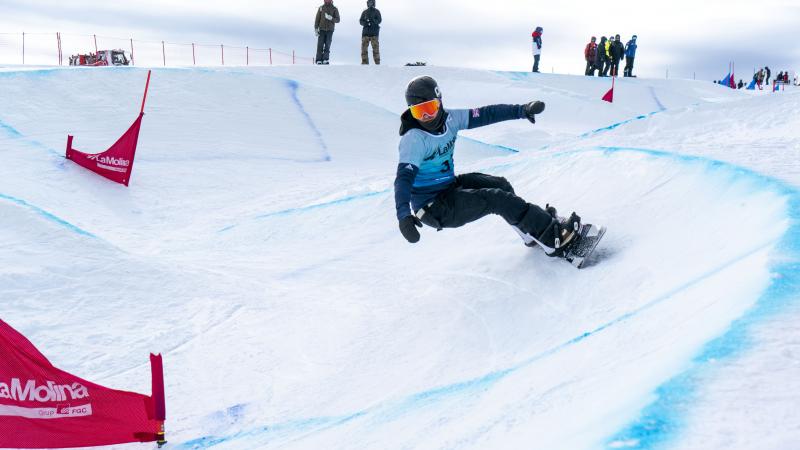 A male Para snowboarder competing being observed by eight people in the background