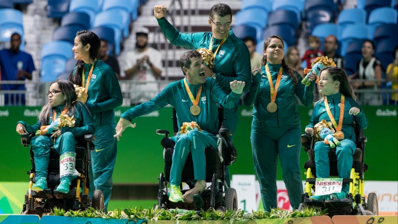 Six people on a podium. Three are in wheelchairs, three are standing behind them