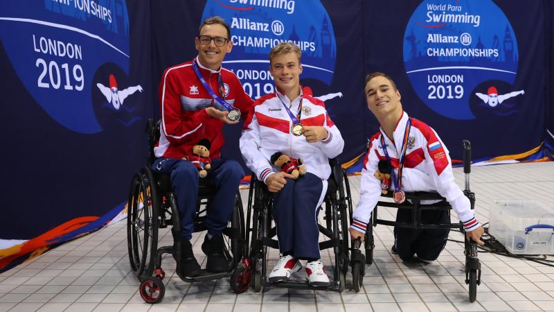Three men in wheelchairs showing their medals