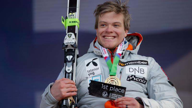 A man with a gold medal smiling and holding a skiing