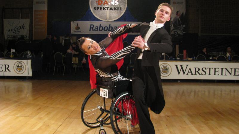 A standing man dancing with a woman in a wheelchair