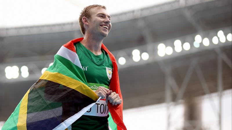 A smiling man with the flag of South Africa around his shoulders 