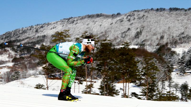 A man skiing wearing a green outfit and sunglasses