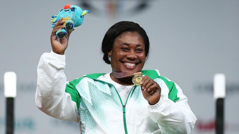 A woman holding a mascot with the right hand and showing the medal with her left hand