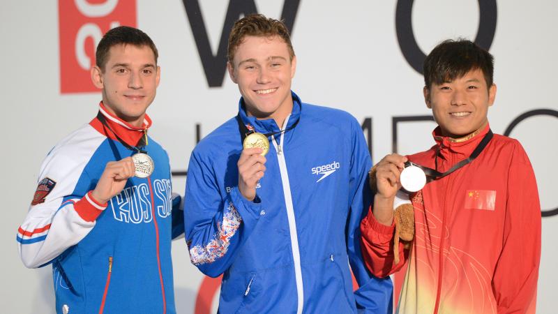 Three male swimmers smile holding their medals