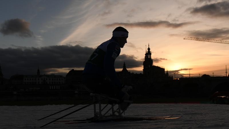 A male sit-skier competing on the snow with the Dresden skyline as background