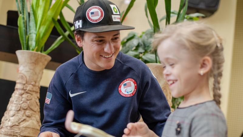 A man wearing a black cap talking to a little girl