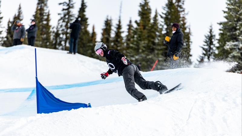 A male Para snowboarder competing being observed by three people