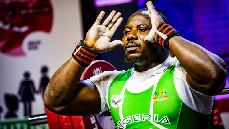 A male powerlifter with his hands in front of the face and a bar with discs behind him