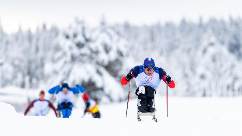 A male sit-skier competing in Para cross-country followed by three competitors