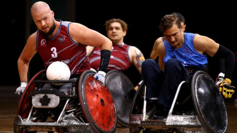 Male wheelchair rugby player moves with ball in his lap