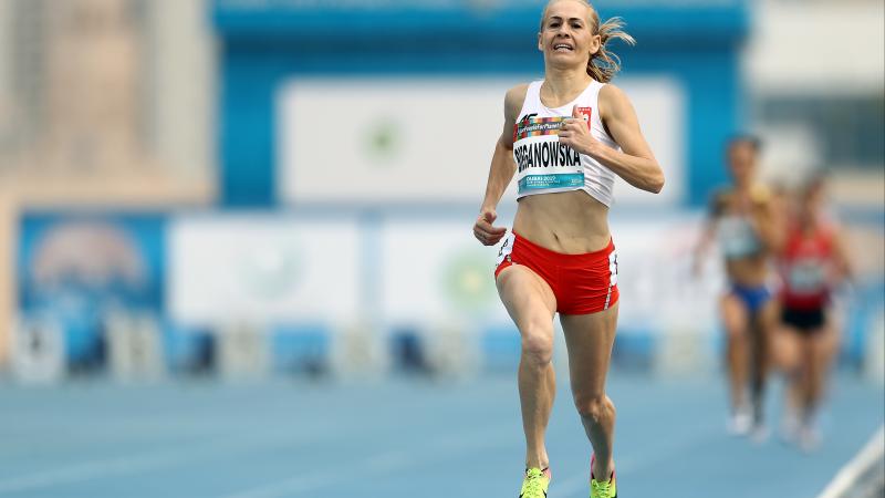 A female runner wearing Poland's uniform running on a blue track