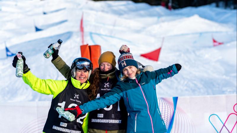 Three female Para snowboarders hugging and posing for a picture