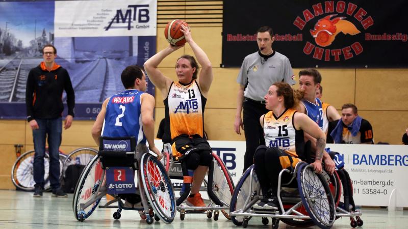 Female wheelchair basketball player holds ball over her head looking to pass