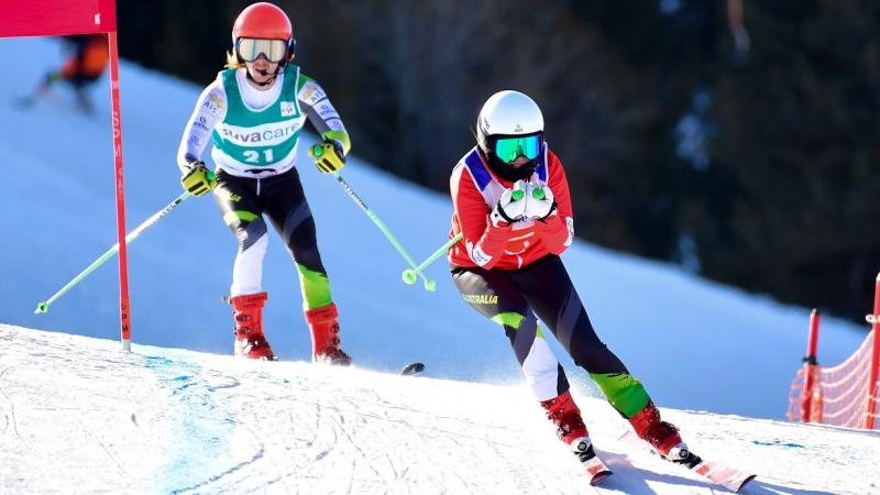 A female guide alpine skier ahead of a male Para alpine skier on a slope