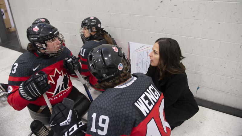 A woman talking to two women in hockey sledges