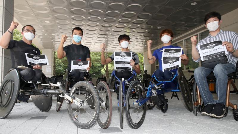 Five Korea wheelchair racers hold fists up with signs supporting Black Lives Matter