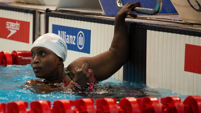 A female swimmer with her left hand on the board looking towards the  pool