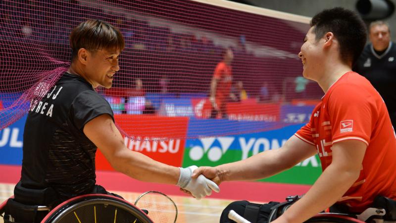 Two male Asian badminton players in wheelchairs shake hands
