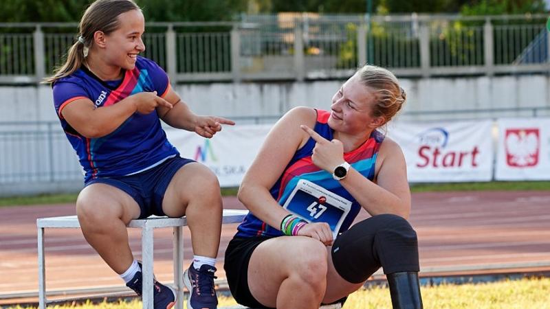 A short stature woman and a woman with a prosthetic leg point at each other