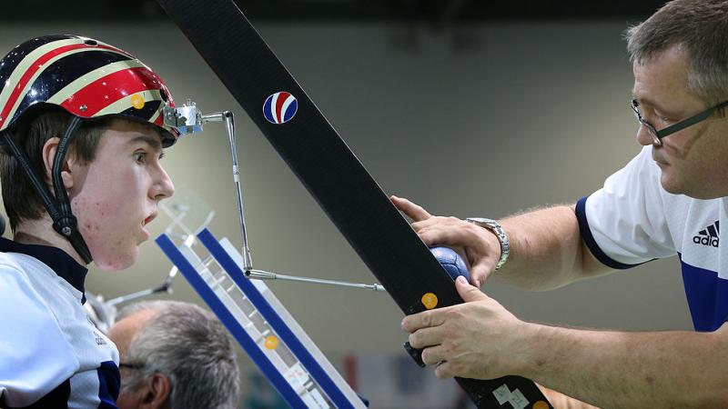 El atleta masculino de Boccia usa un puntero para golpear la pelota con su asistente ajustando la rampa