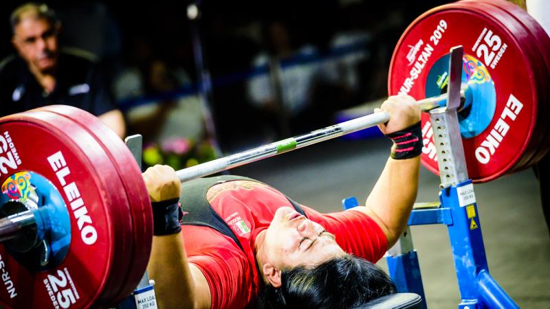 A female powerlifter competing being observed by a man in a chair