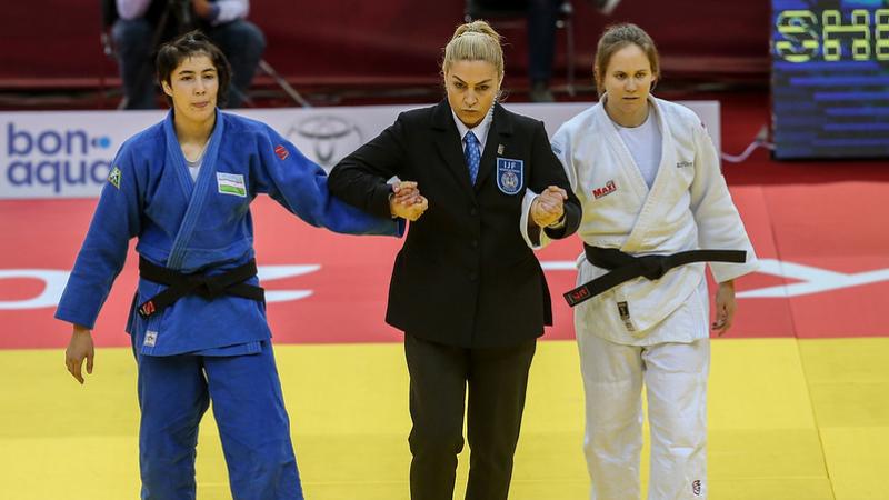Referee holding the arms of two female judoka as she prepares to announce the winner